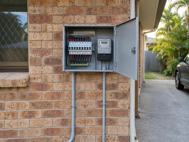Exterior switchboard and meter box on a brick wall beside a driveway in Coombabah